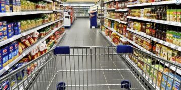 Supermarket aisle with consumer goods viewed from a shopping cart.
