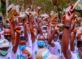 Group of NYSC members raising booklets outdoors, wearing white shirts