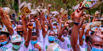 Group of NYSC members raising booklets outdoors, wearing white shirts