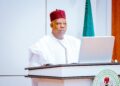 Vice President Kashim Shettima in white traditional attire with Nigerian flags behind him